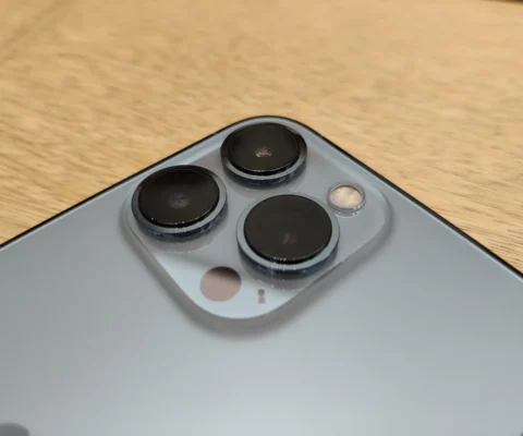 Un gros plan montre le module de caméra arrière d'un smartphone gris sur une surface en bois clair.