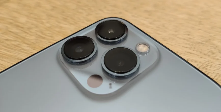 Un gros plan montre le module de caméra arrière d'un smartphone gris sur une surface en bois clair.