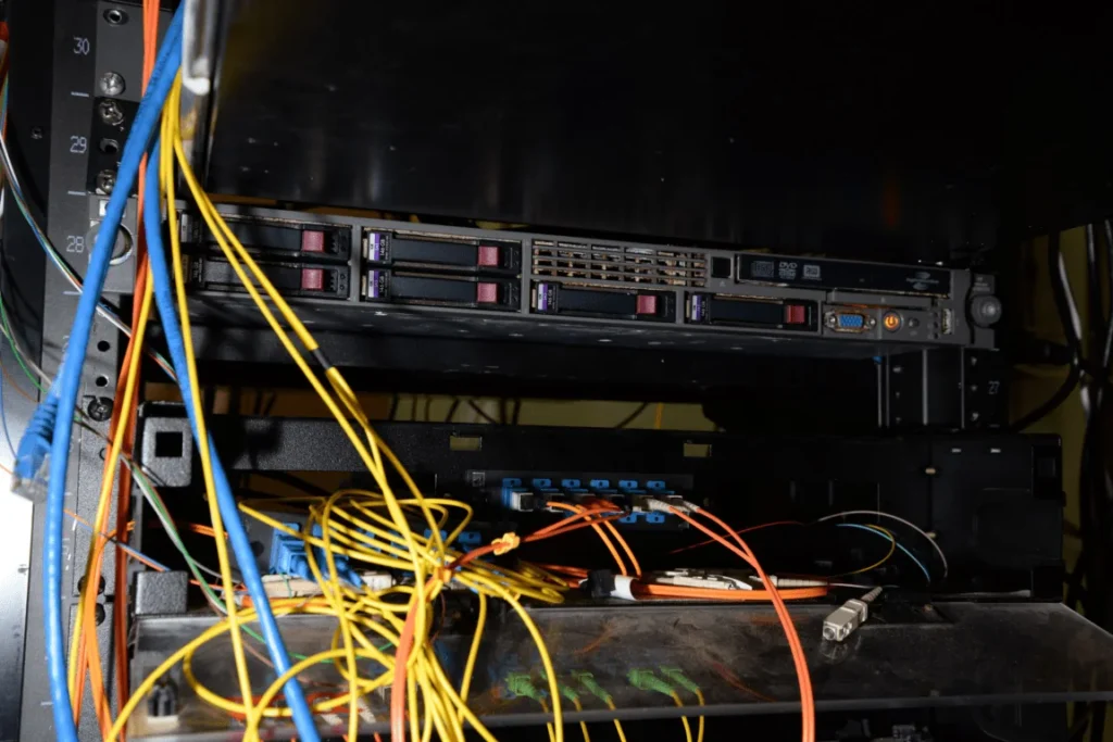 Vue rapprochée d'un rack de serveurs rempli de câbles et d'équipements informatiques.