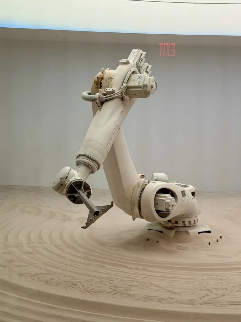 Un bras robotique industriel est exposé dans un espace d'exposition blanc, posé sur un sol texturé.