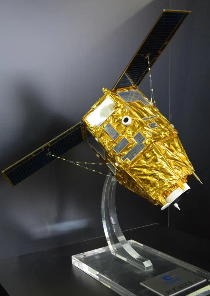 Une maquette d'un satellite doré avec des panneaux solaires est présentée sur un socle en acrylique.