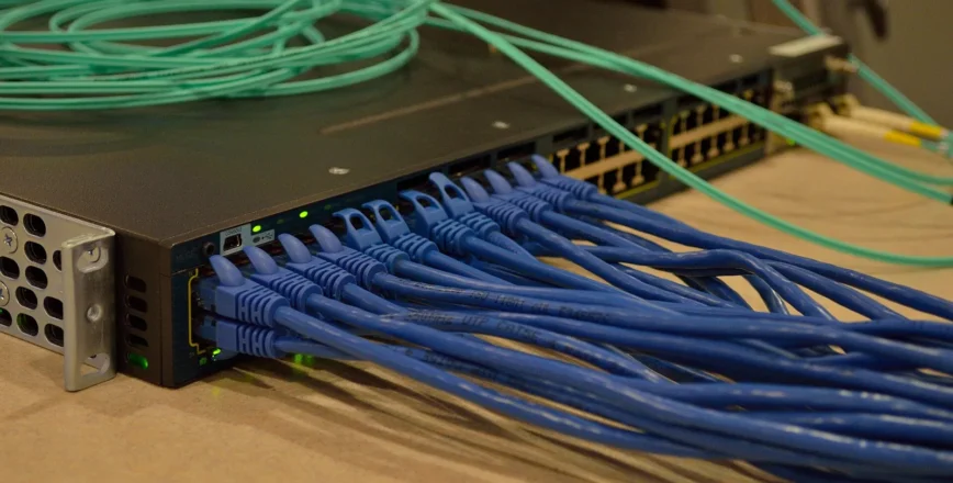 Un ensemble de câbles réseau bleus sortent d'un rack serveur gris sur une surface claire.